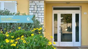 L'ingresso di un edificio con muro in pietra, porta in vetro e un cartello che indica il prezzo per una stanza con balcone e due letti.