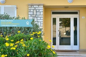 L'ingresso di un edificio con muro in pietra, porta in vetro e un cartello che indica il prezzo per una stanza con balcone e due letti.
