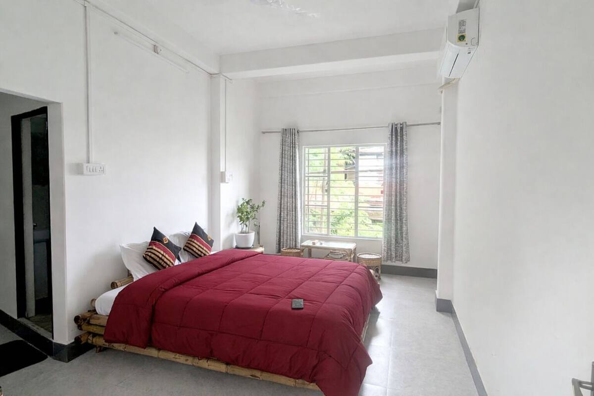 A bedroom with a bed, a window, a small table, and a potted plant.