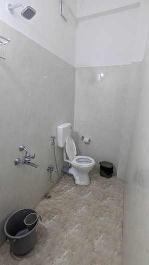 A small bathroom with a toilet, a shower, and a bucket. - Kamakhya Homestay by Bonoriya (Guwahati)