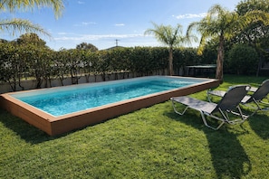A rectangular swimming pool with a wooden border, surrounded by a well-maintained lawn and trees. - Villa Paionia/ Heated Pool/ Sea View/ Private Resort (Anavissos)