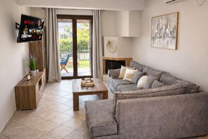 A living room with a grey sofa, a wooden coffee table, a TV on the wall, and a balcony with a view of greenery. - Villa Paionia/ Heated Pool/ Sea View/ Private Resort (Anavissos)