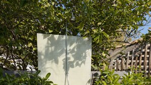 A small, enclosed outdoor shower area with a wooden deck and surrounding greenery.