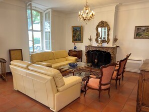 A living room with a sofa, chairs, a fireplace, and a chandelier. - Maison de Famille du XIX° siècle - Property in Terre de PROVENCE- swimming pool (Saint-Chamas)