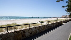 Une route côtière bordée d’un mur de pierres, avec une plage et une jetée en arrière-plan.