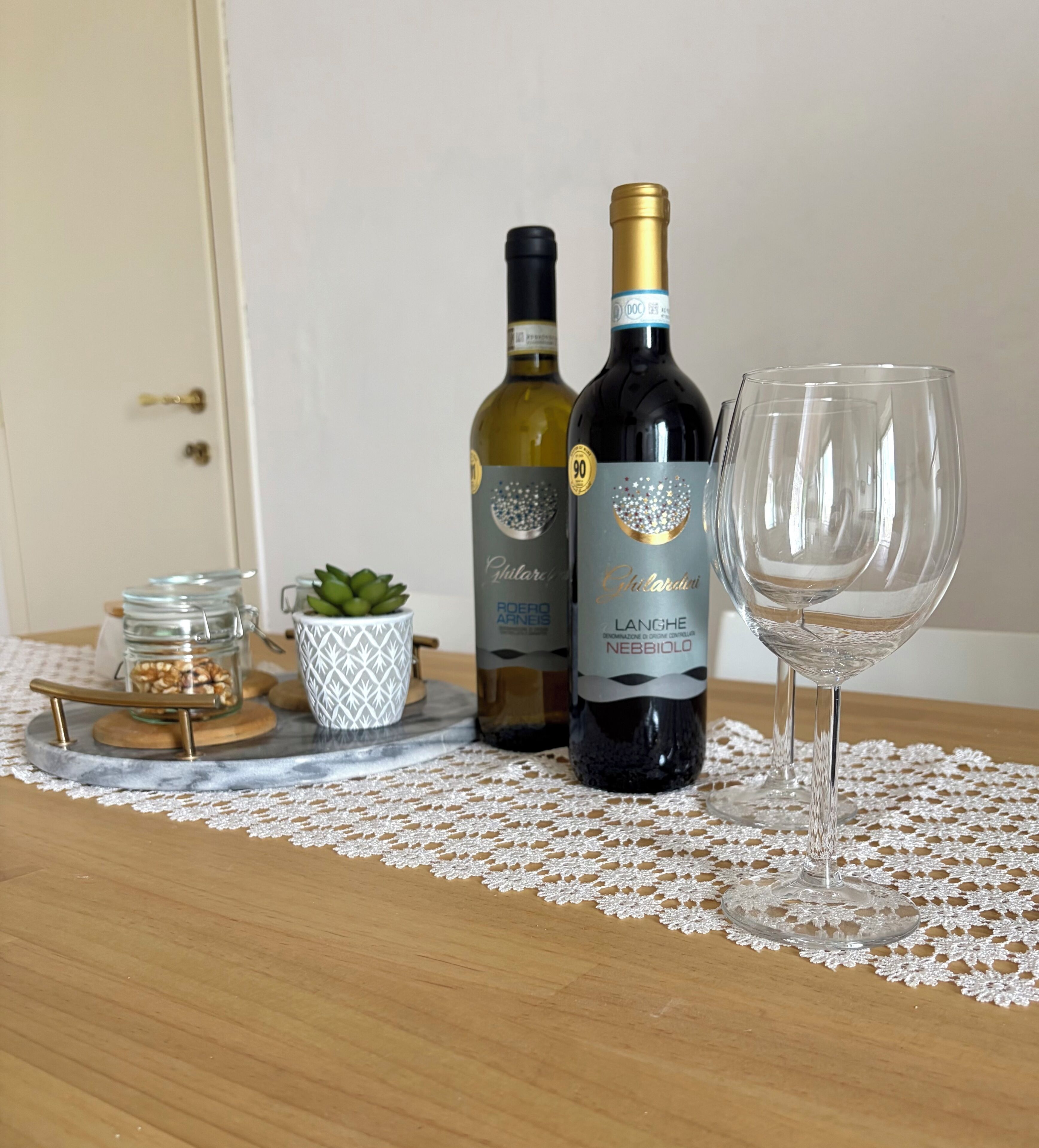 A table with two wine bottles and a glass on a lace doily.
