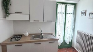 Pieni, käytännöllinen keittiö, jossa on kaasuliesi, pesuallas ja valkoiset kaapit.