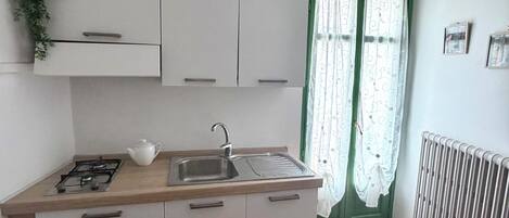 Una cocina compacta con estufa a gas, lavamanos y gabinetes blancos.