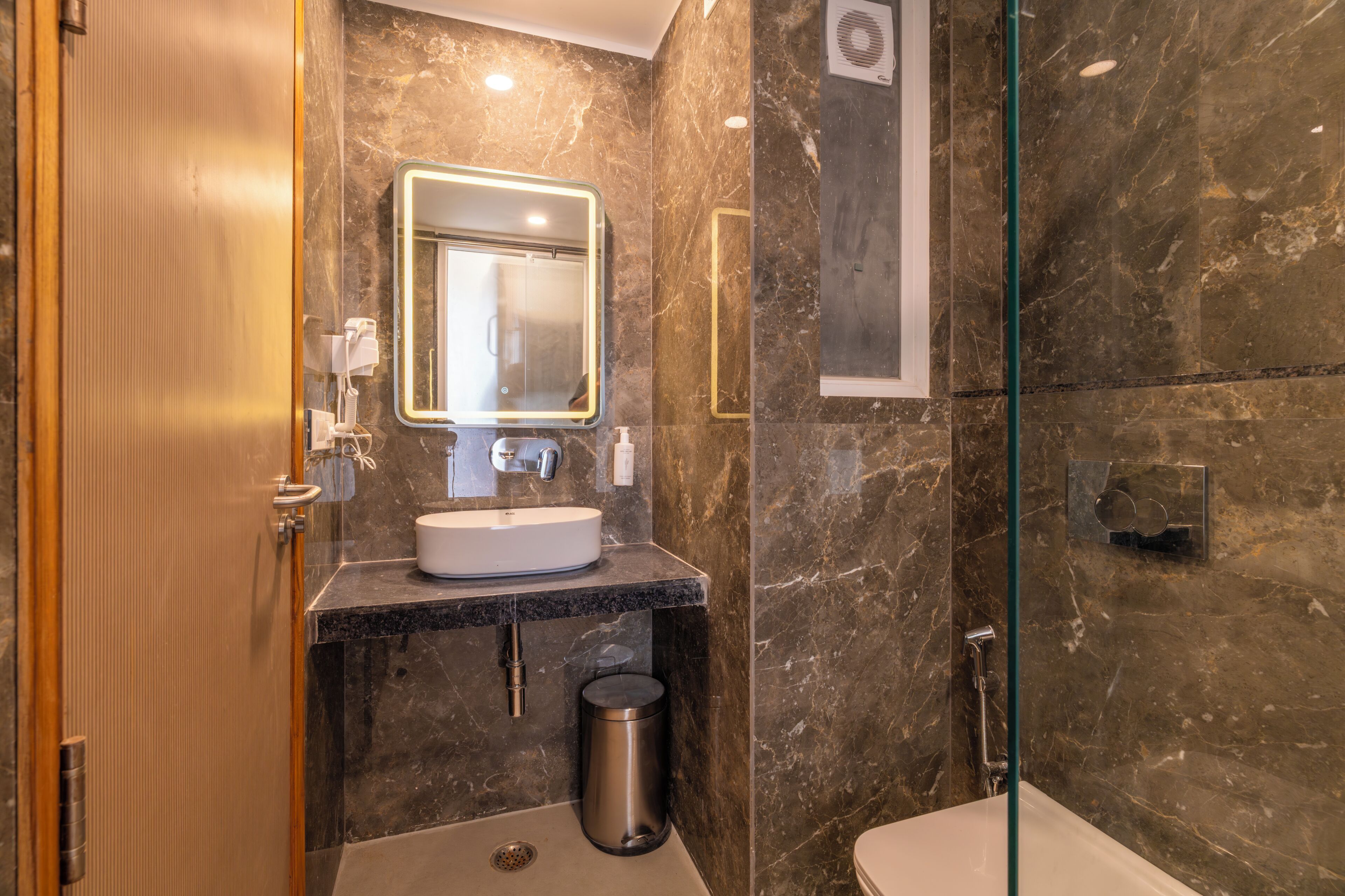 A modern bathroom with a marble wall, a sink with a mirror, a glass shower enclosure, and a toilet.