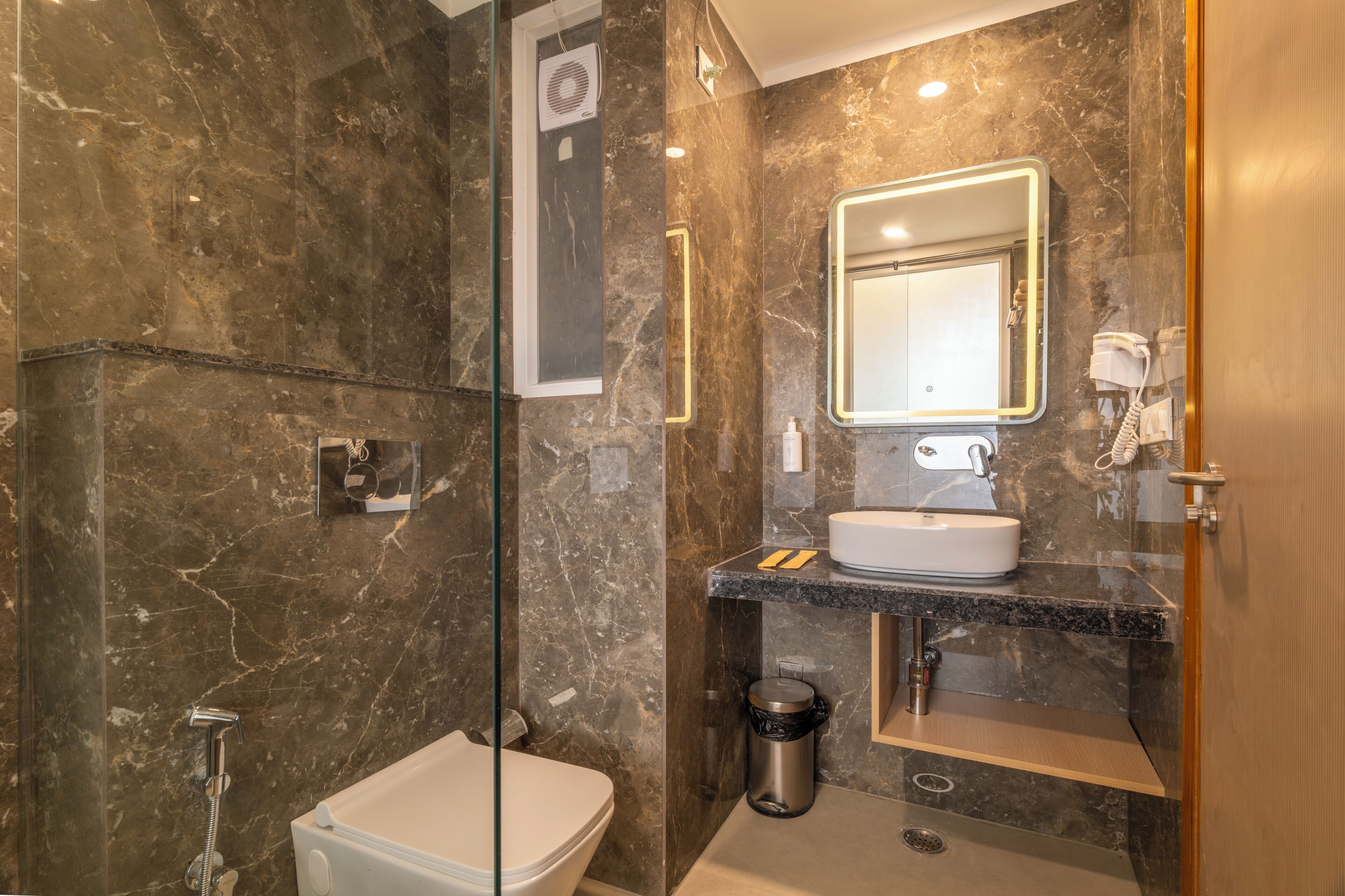 Un baño moderno con cabina de ducha de vidrio, inodoro blanco, lavabo con espejo y un perchero para toallas.