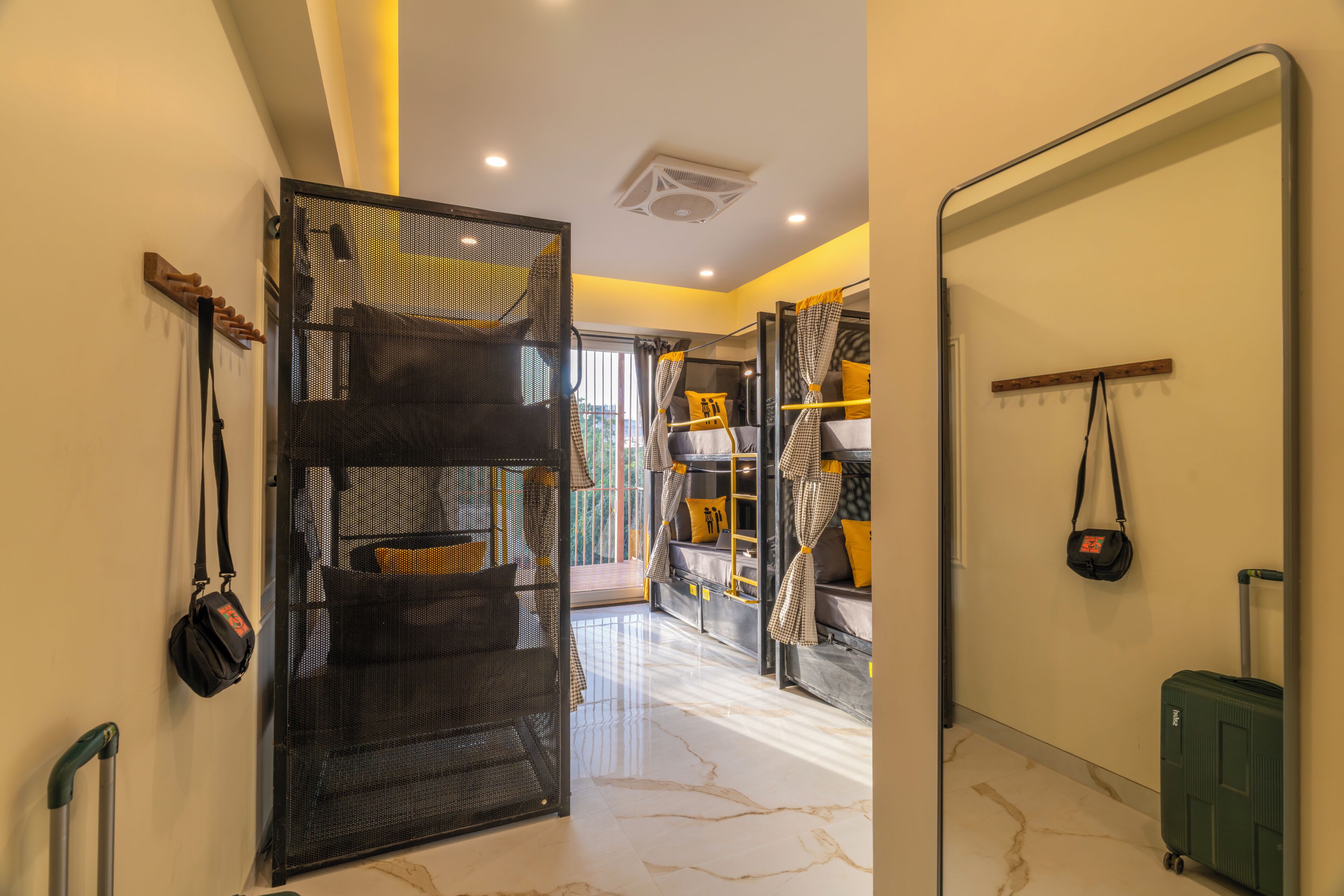 Quarto de hotel com uma cama, uma mala, um suporte de bagagem na parede e uma porta que dá para outro quarto.