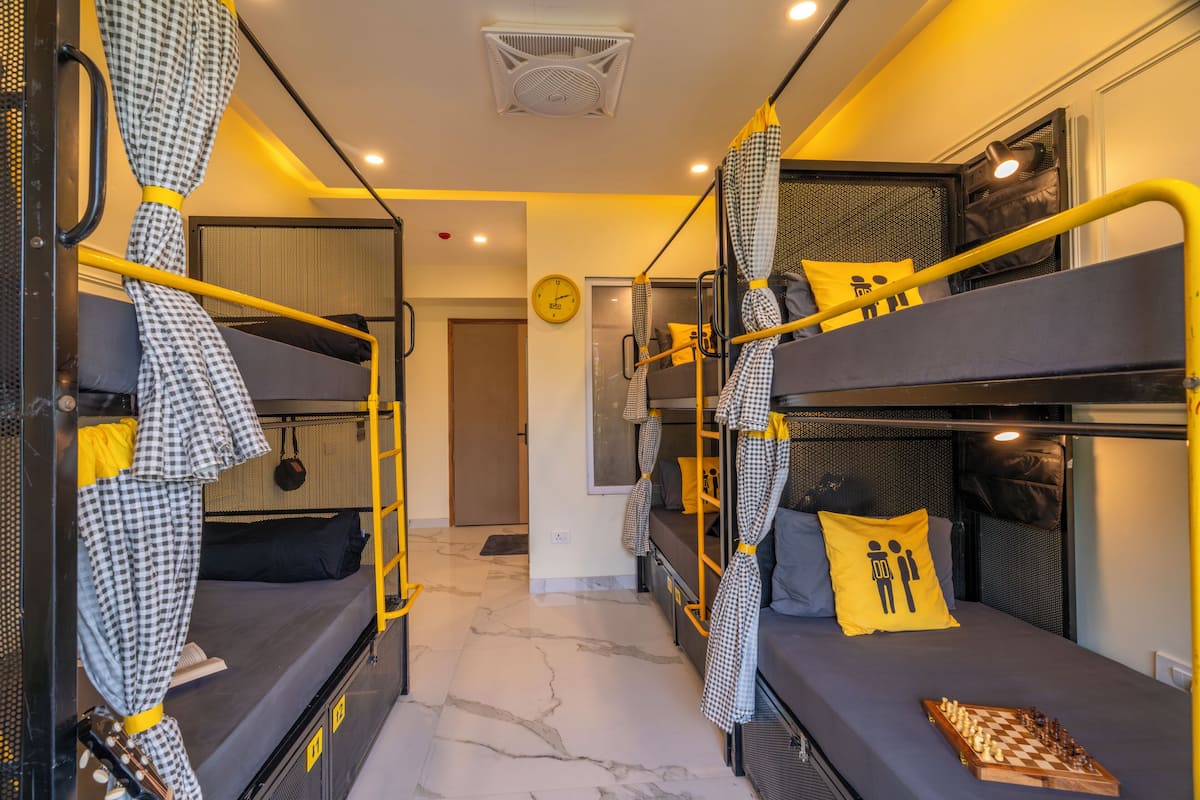 A compact hotel room with bunk beds, a chessboard, a clock, and a door.