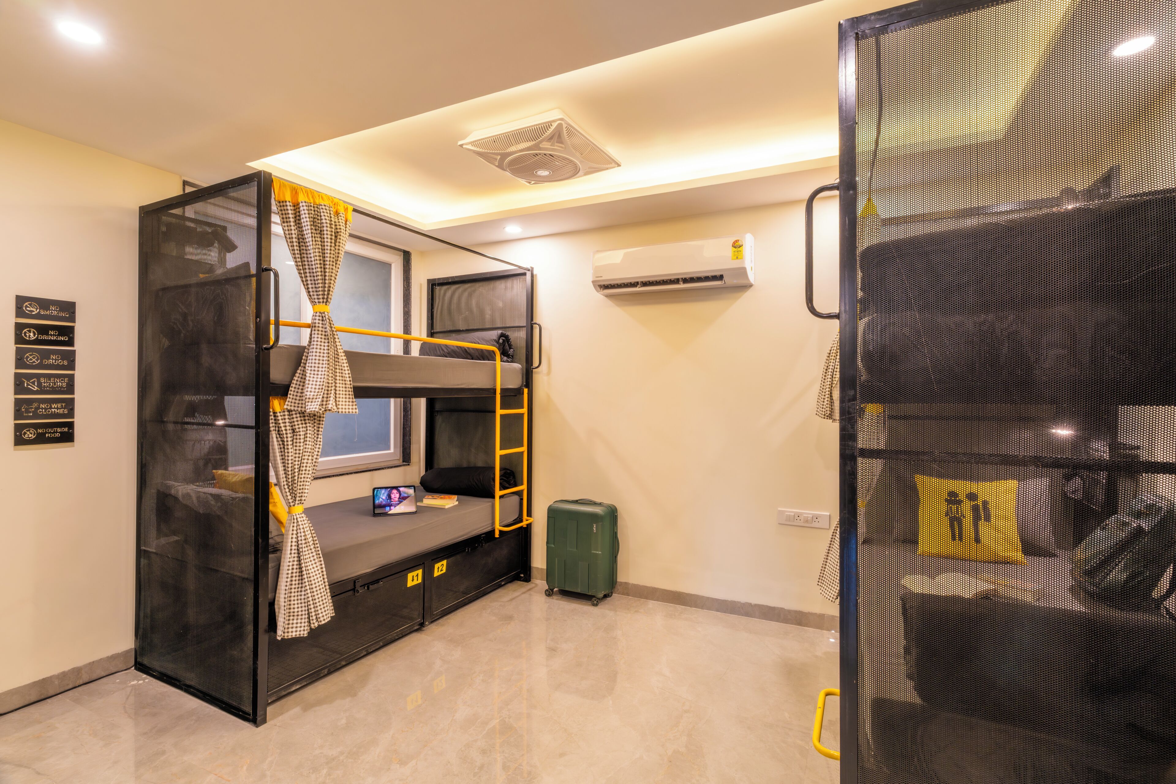 A bunk bed room with a desk, a laptop, a suitcase, and an air conditioning unit.