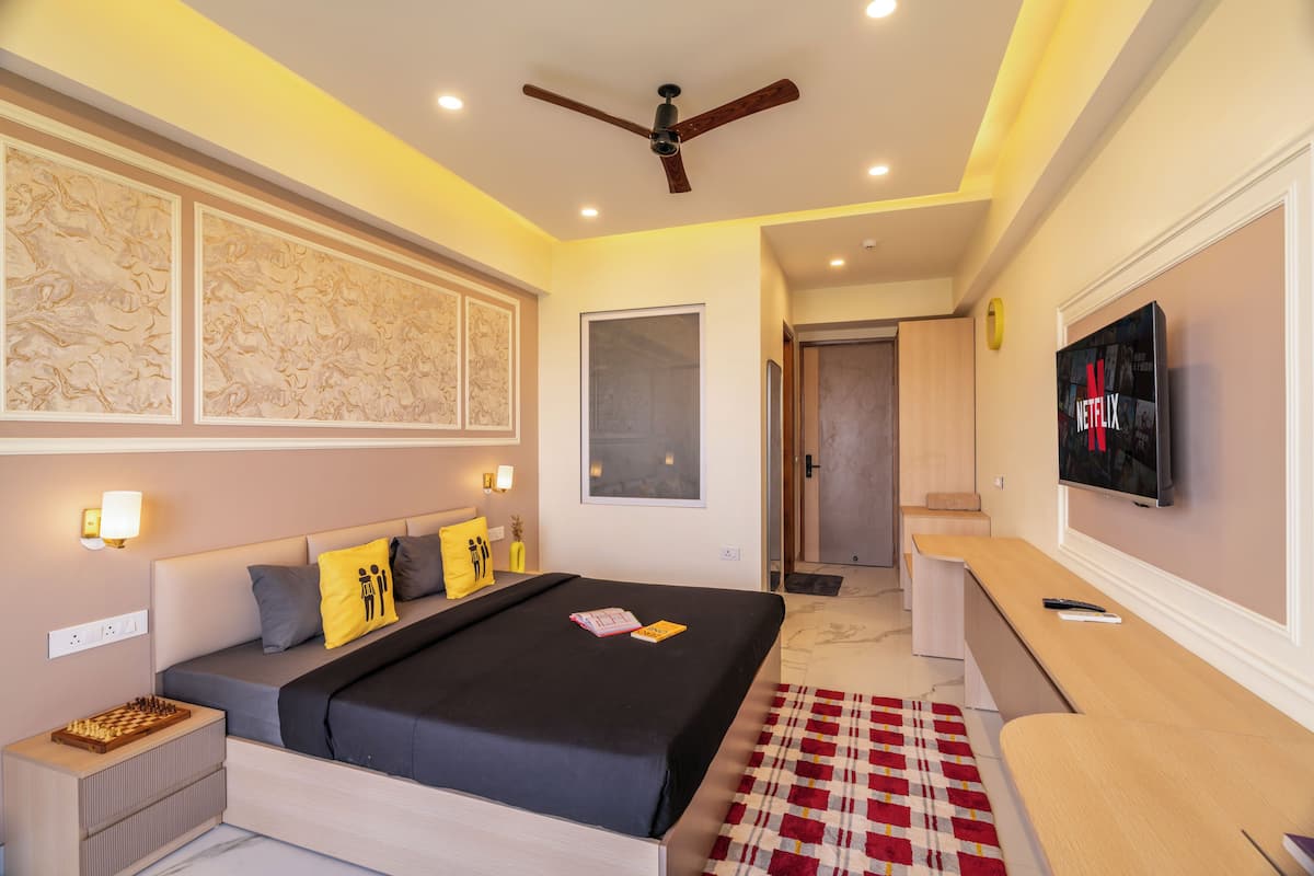 A modern hotel room with a large bed, bedside tables, a TV, and a ceiling fan.