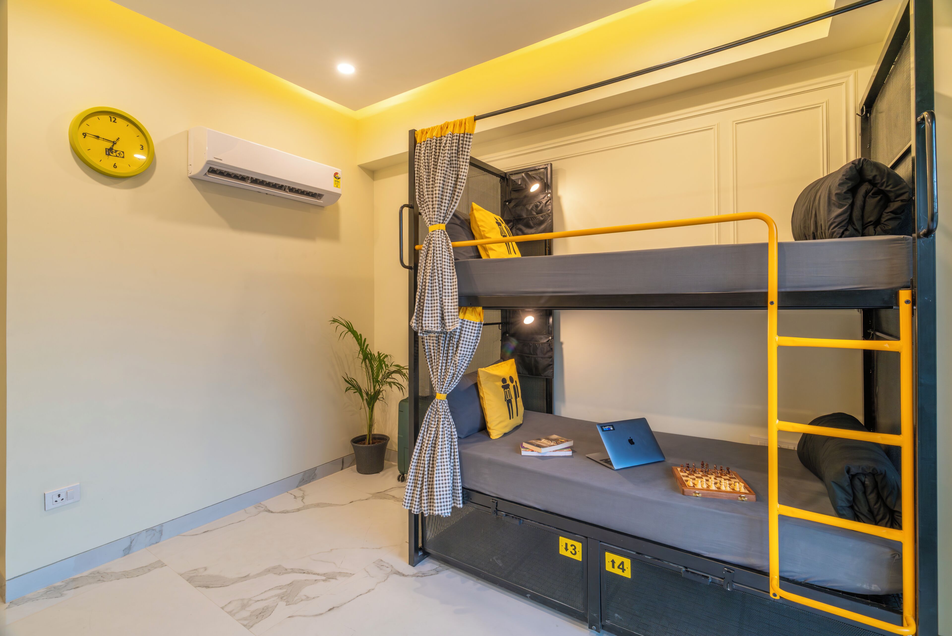 Una cama litera con una computadora portátil y un tablero de ajedrez, un reloj y un aire acondicionado en la pared.