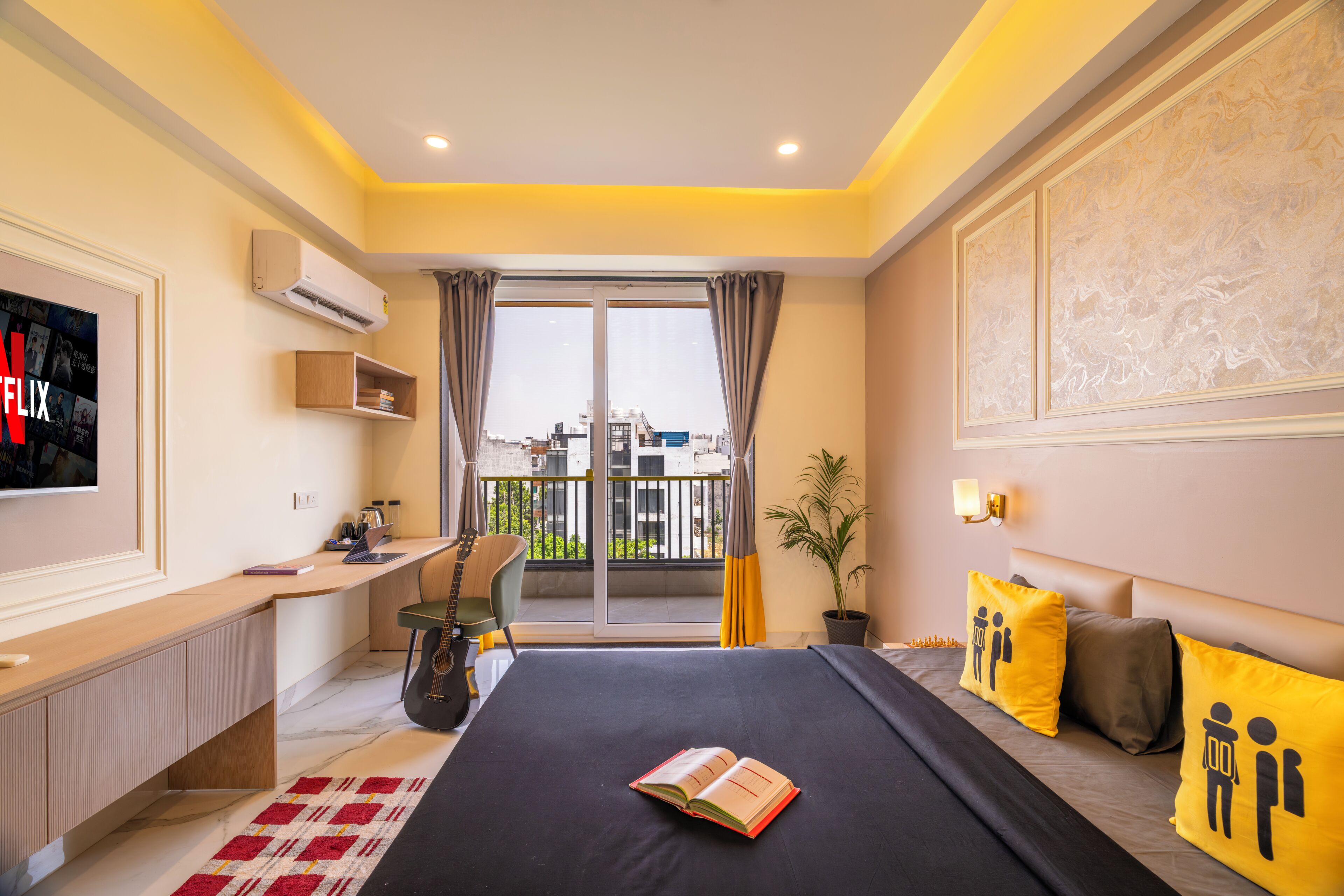 Ein modernes Hotelzimmer mit Bett, Schreibtisch, Fernseher, einem Balkon mit Aussicht und einer Zimmerpflanze.