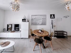 Ein moderner Essbereich mit einem runden Holztisch, schwarzen Stühlen und einem weißen Sideboard mit einem Fernseher.