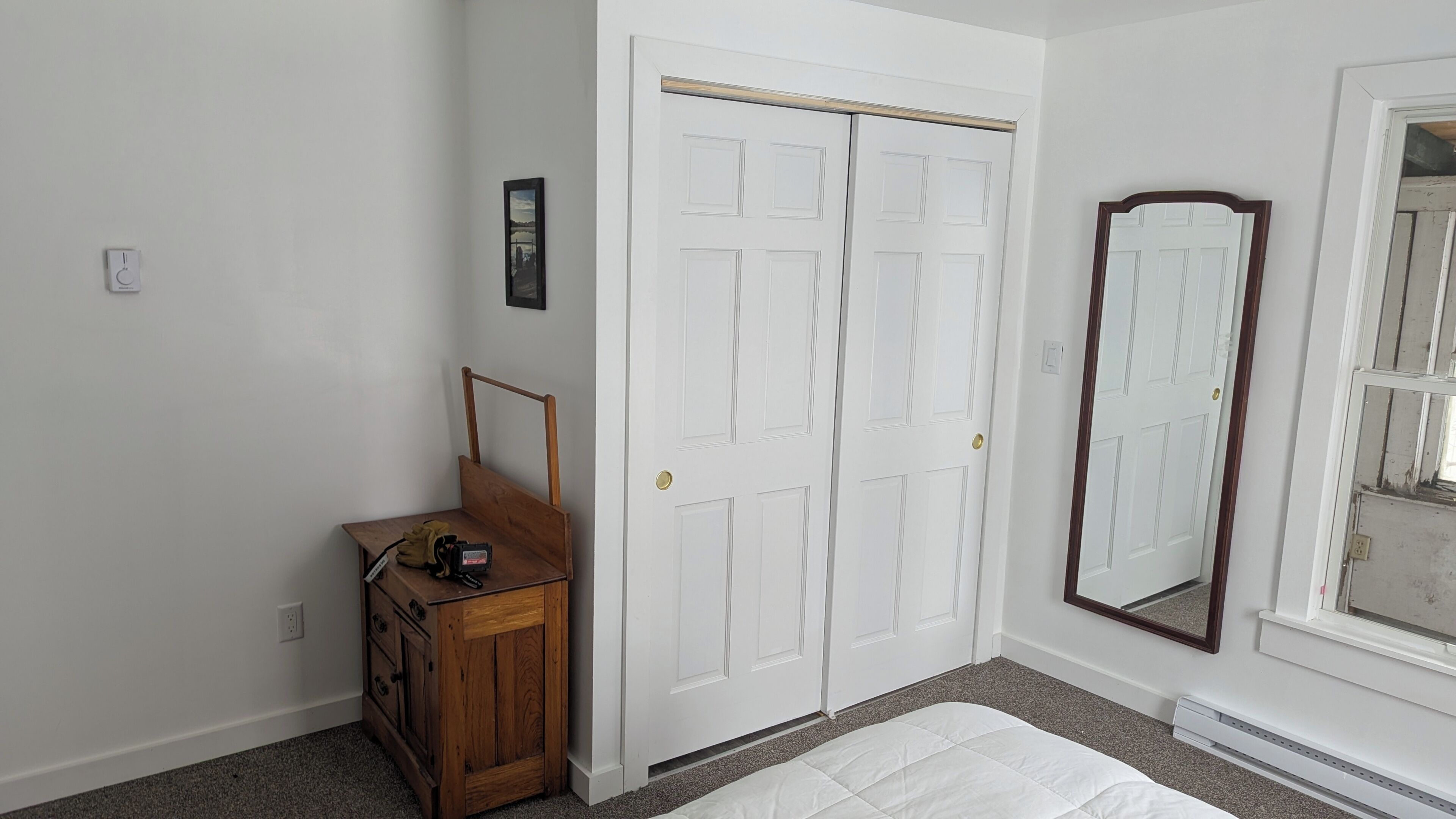 Une chambre avec une porte blanche, une commode en bois, un miroir et un lit.