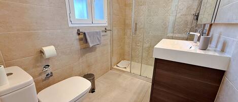 A bathroom with a toilet, a shower, a sink, and a window.
