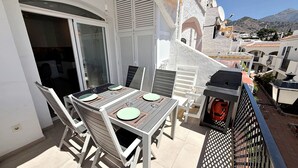 Varanda com mesa posta para dois, móveis de jardim e churrasqueira.
