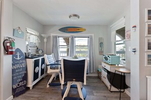 A compact kitchen with a dining area, a surfboard decoration, and a small table with a radio. - 5600 Seaview Ave, Unit 34 (Wildwood Crest)
