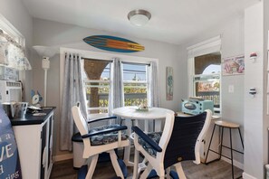 Une cuisine compacte avec une table ronde, deux chaises, un petit tabouret de bar, une décoration sur le thème du surf et une radio ancienne.