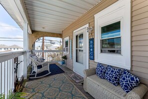 A covered porch with a rocking chair, a bench, and a welcome mat.