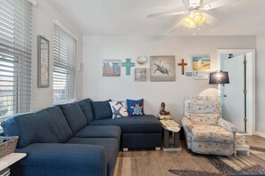 Un salon avec un canapé bleu foncé, une petite table d’appoint, un fauteuil décoratif et divers éléments décoratifs muraux, notamment un tableau représentant une croix et un autre représentant une tortue.