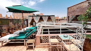 A rooftop terrace with lounge chairs, a table, and a green umbrella. - Riad jamaique (Marrakech)
