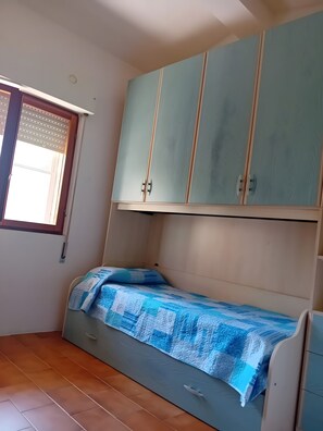 Una habitación con cama, ventana con persianas y un armario azul claro.