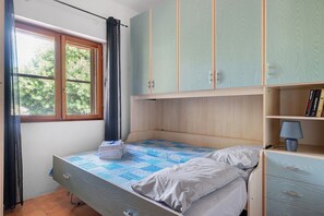 Ein Schlafzimmer mit einem Einzelbett, einem Fenster mit Vorhängen, einem Kleiderschrank und einem Nachttisch mit Lampe.