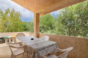 Eine Terrasse im Freien mit Tisch und Stühlen, umgeben von einer gemauerten Wand und Bäumen.
