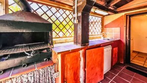 Een buitenkeuken met een barbecue, een spoelbak en een raam met uitzicht op een tuin.