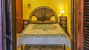 Een bed met een geweven hoofdbord, een bed met een patroon en een klein nachtkastje met een lamp.