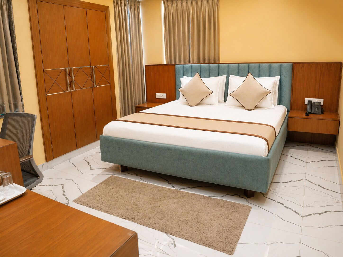 A hotel room with a bed, bedside table, and a desk with a chair.