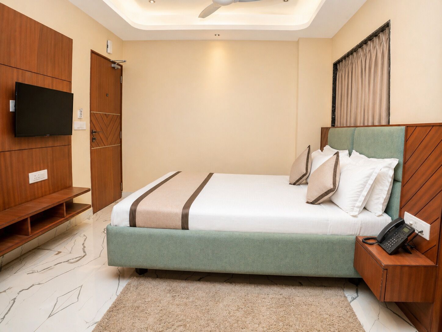 A modern hotel room with a bed, a TV, a wardrobe, and a bedside table with a phone.