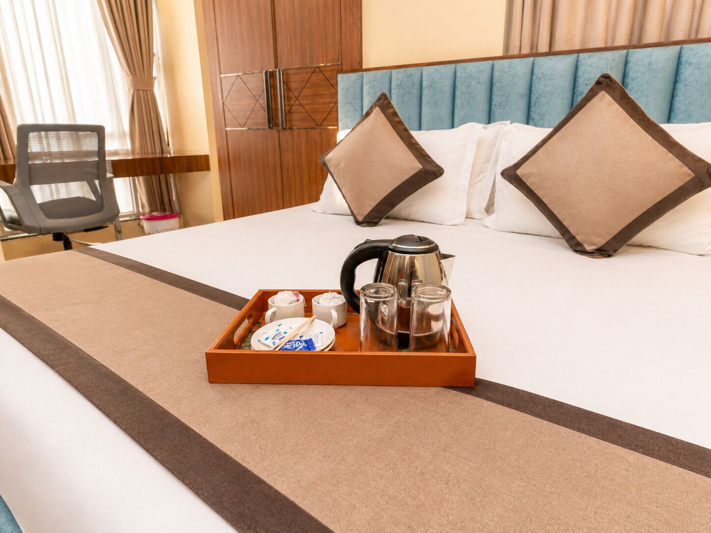 A hotel room with a bed, a tray with breakfast items, a kettle, and a chair.