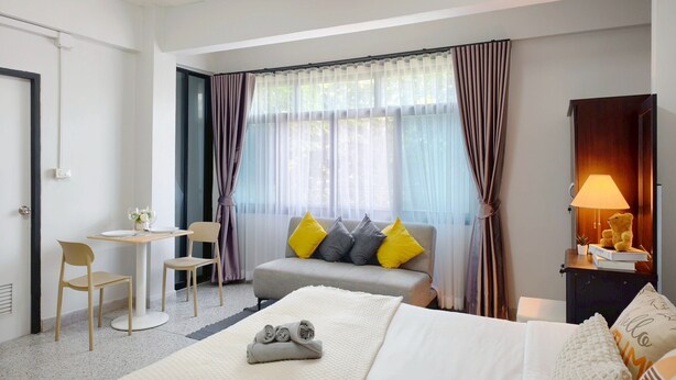 A hotel room with a bed, a desk, a chair, a sofa with cushions, a window with curtains, and a lamp. - Xin Hotel at Udomsuk 29 (Bangkok)