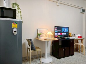 Une chambre de taille modeste équipée d’un four à micro-ondes, d’une petite télévision, d’un bureau avec une lampe, d’une chaise et d’un placard.