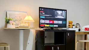 A television on a stand with a selection of apps, a lamp, a teddy bear, and a small plant. - Xin Hotel at Udomsuk 29 (Bangkok)