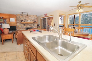 A kitchen with a large sink, wooden cabinets, a stone wall, and a view of the outdoors.