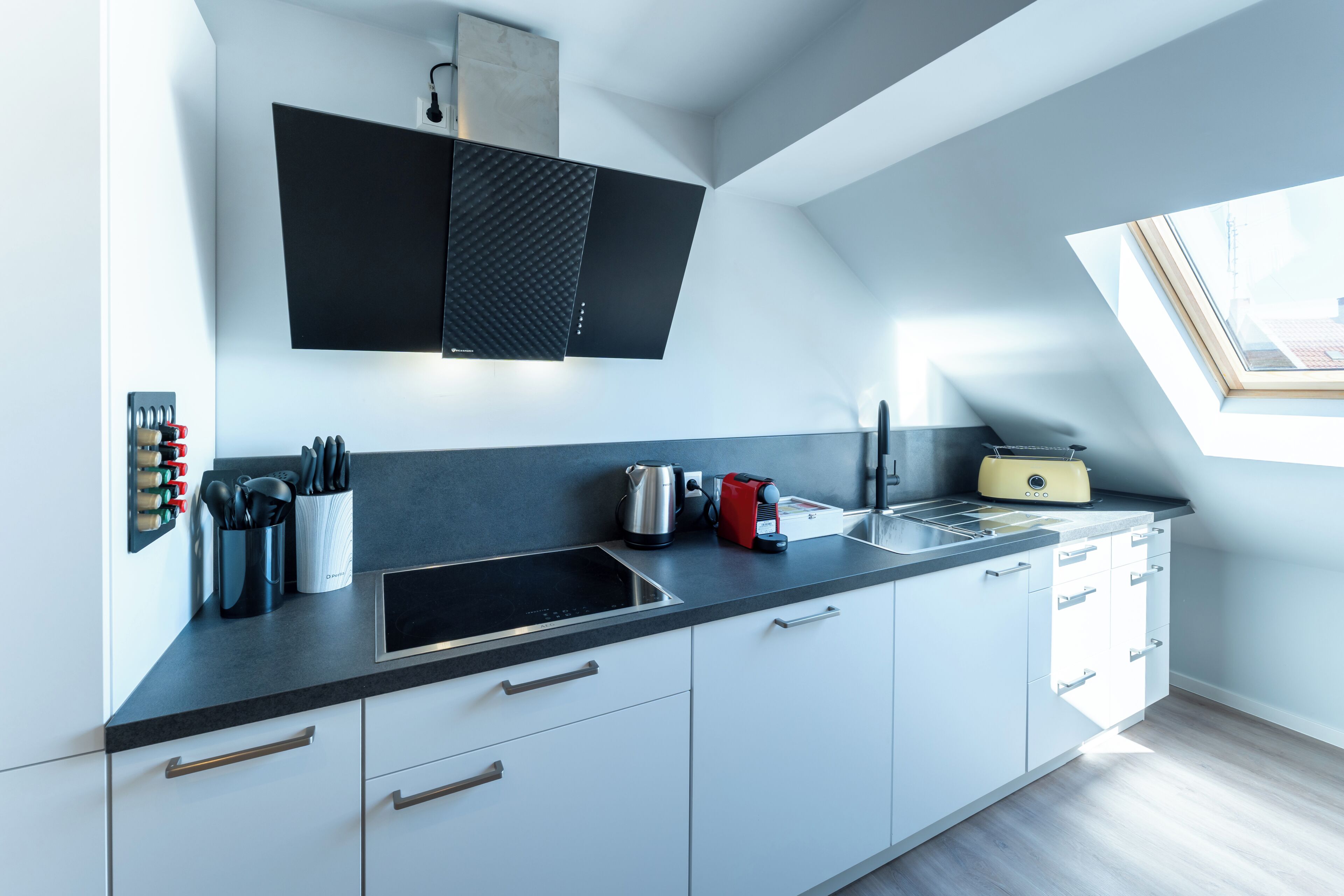 Une cuisine moderne avec un plan de travail noir, des armoires blanches, une cuisinière encastrée et une lucarne.