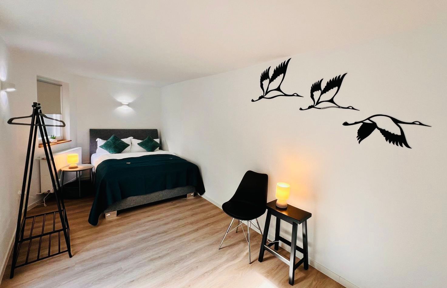 A bedroom with a bed, bedside table, chair, lamp, and wall art.
