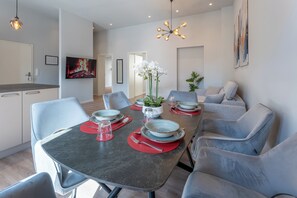 A modern dining area with a round table, grey chairs, and a chandelier.