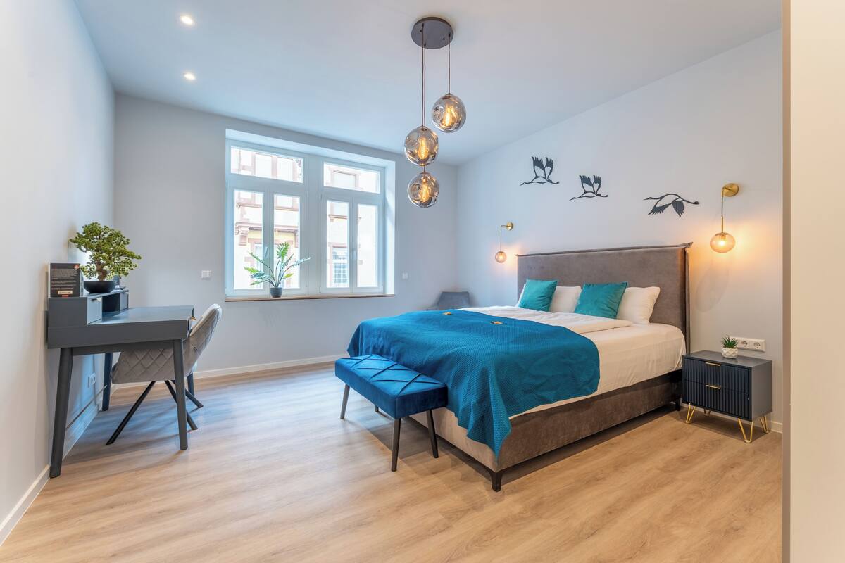 A modern bedroom with a bed, desk, chair, and a window with a view.