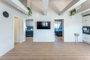 Una sala de estar moderna con televisor de pantalla plana, piso de madera y una escalera que lleva a un dormitorio.