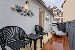 An outdoor patio with two black wicker chairs, a small table, and a decorative wall art piece. - Lit Living Worms (Worms)