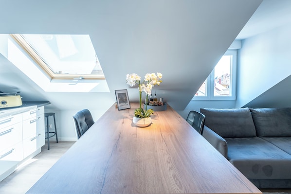 A modern loft bedroom with a skylight, a dining table, a sofa, and a potted orchid.