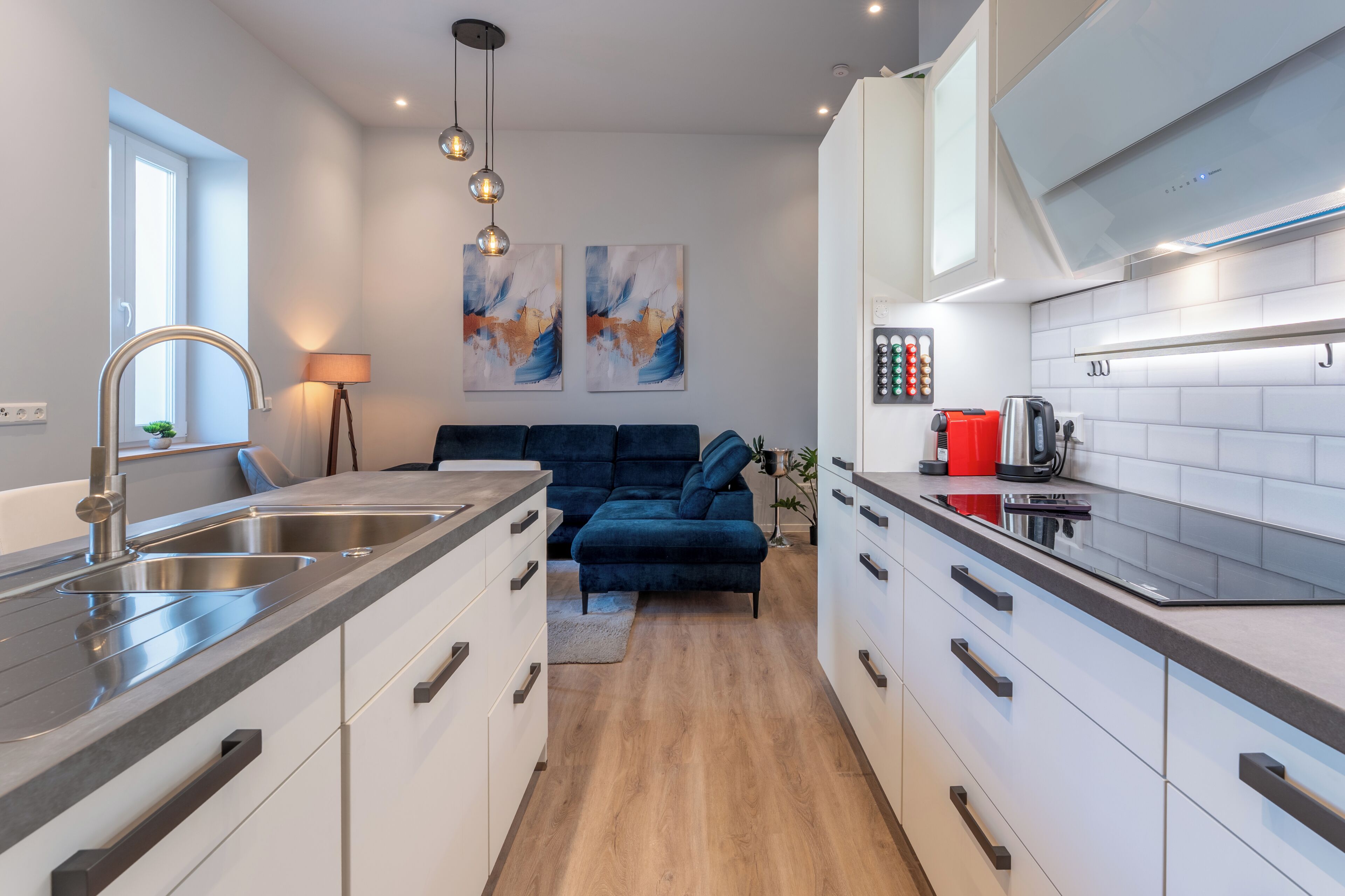 A modern kitchen with a central island, white cabinetry, and a blue sofa in the living area.