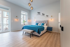 A bedroom with a bed, bench, bedside tables, wall art, and a window.